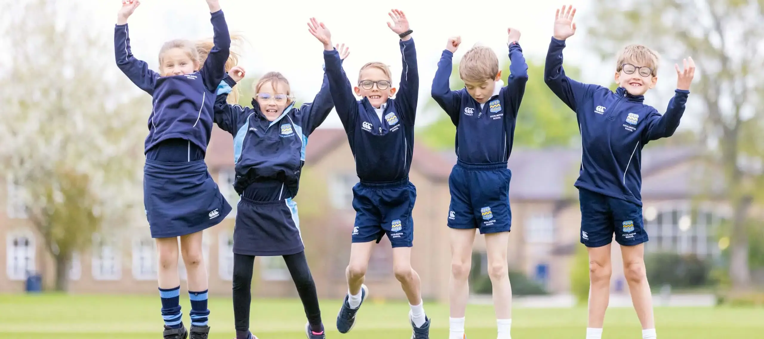 Pocklington Prep pupils jumping and raising their hands on the campus grounds 