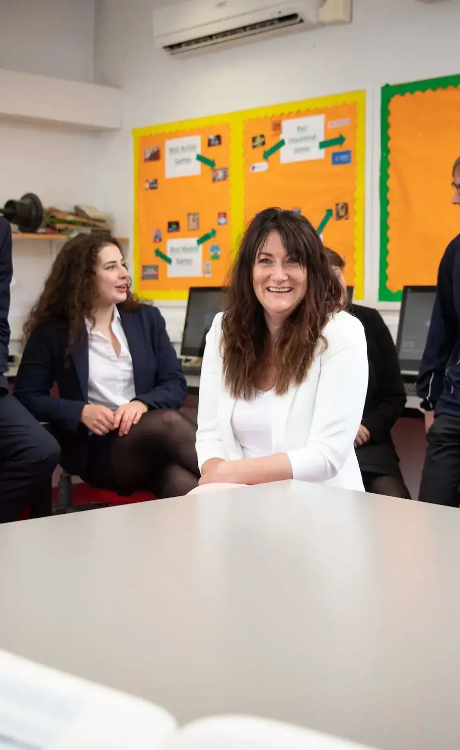 Teacher sat at desk in classroom surrounded by Sixth Form pupils